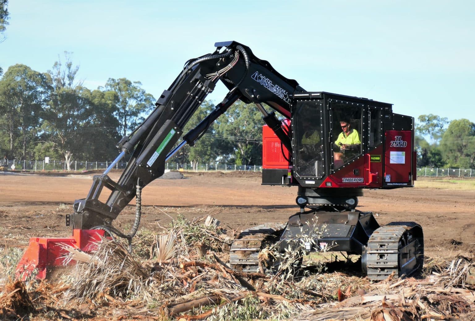 Land clearing contractor using a machine to move trees and branches from a paddock.